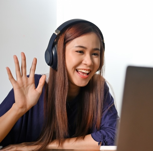 high school girl wearing headphones and waving at online tutor