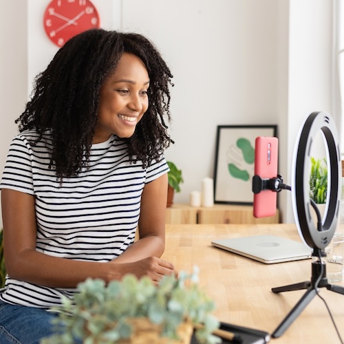 high school girl recording content on her phone at a table with a ring light
