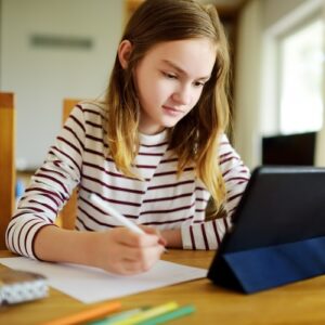 English I: Discovery - Smart preteen schoolgirl doing her homework with digital tablet at home. Education and distance learning for kids. Homeschooling during quarantine.